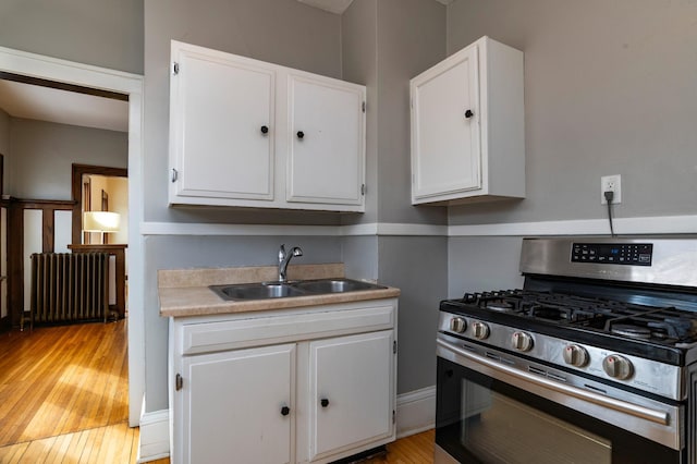 kitchen featuring radiator heating unit, white cabinets, stainless steel range with gas stovetop, a sink, and light wood-type flooring