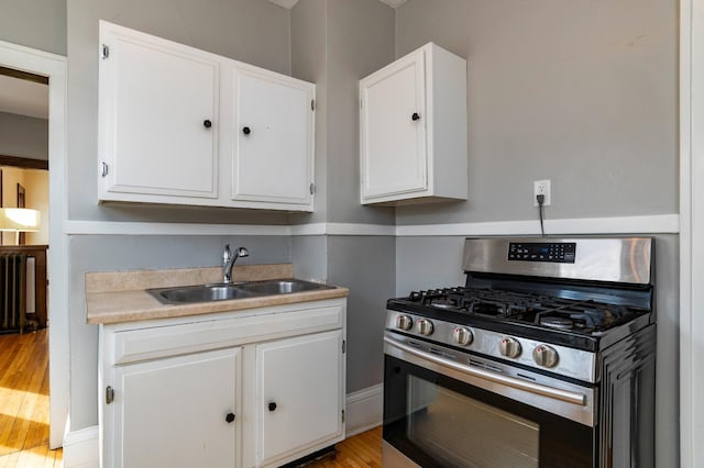 kitchen with a sink, light wood-style floors, white cabinets, light countertops, and stainless steel range with gas cooktop