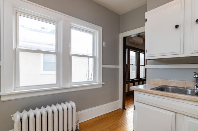 kitchen featuring a sink, white cabinetry, light countertops, radiator, and light wood finished floors