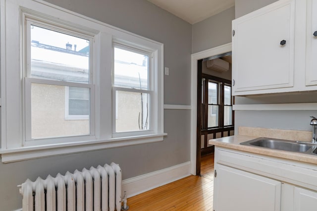 kitchen featuring light countertops, radiator heating unit, white cabinets, a sink, and light wood-type flooring