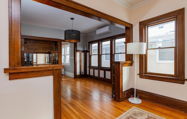 entrance foyer featuring crown molding, light wood-type flooring, a wall mounted air conditioner, and baseboards