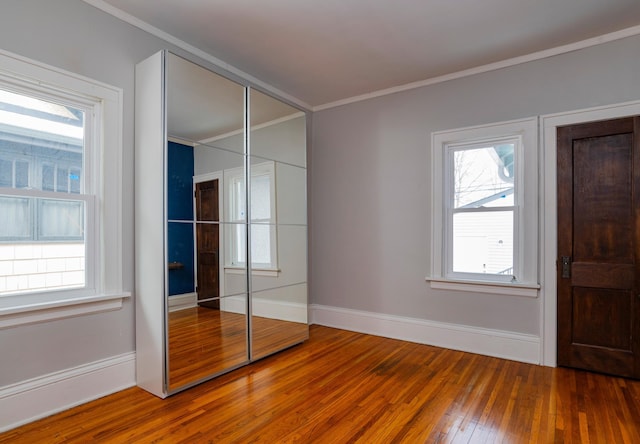 unfurnished bedroom featuring ornamental molding, wood-type flooring, a closet, and baseboards