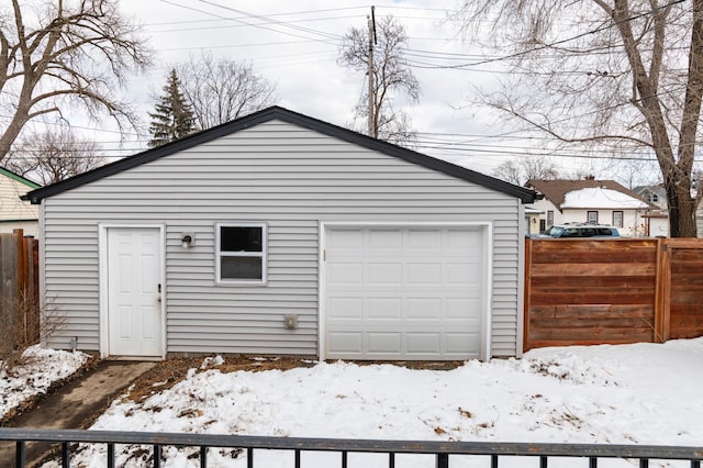 snow covered garage featuring a garage and fence