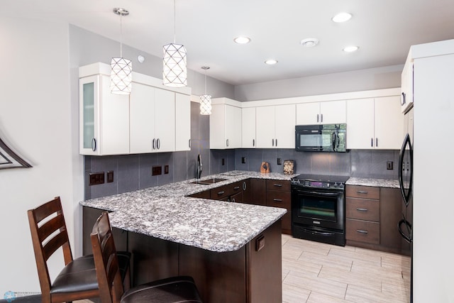 kitchen featuring decorative light fixtures, sink, a breakfast bar area, dark brown cabinetry, and black appliances