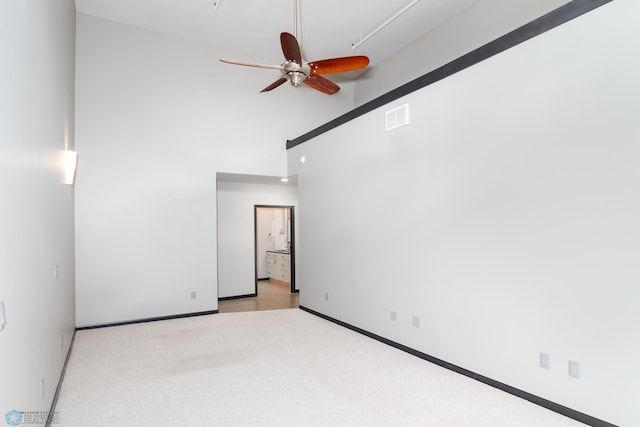 spare room with ceiling fan, light carpet, and a towering ceiling