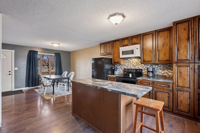 kitchen with dark countertops, dark wood finished floors, a kitchen island, and black appliances