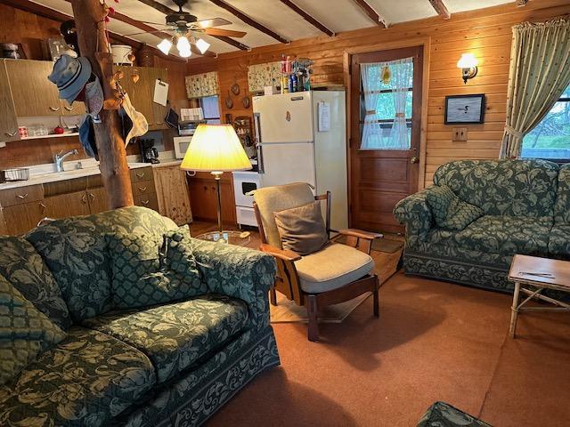 carpeted living room featuring ceiling fan, wooden walls, sink, and beam ceiling