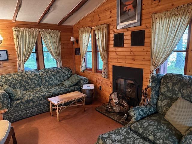 carpeted living room featuring a fireplace, wooden walls, and vaulted ceiling