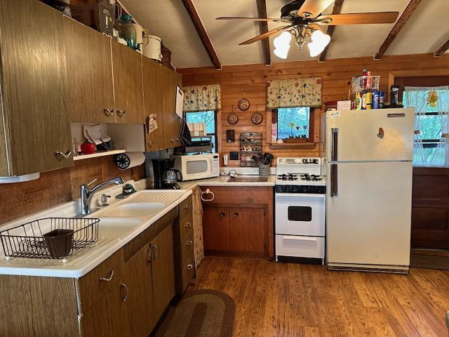 kitchen featuring sink, light wood-type flooring, wooden walls, beamed ceiling, and white appliances