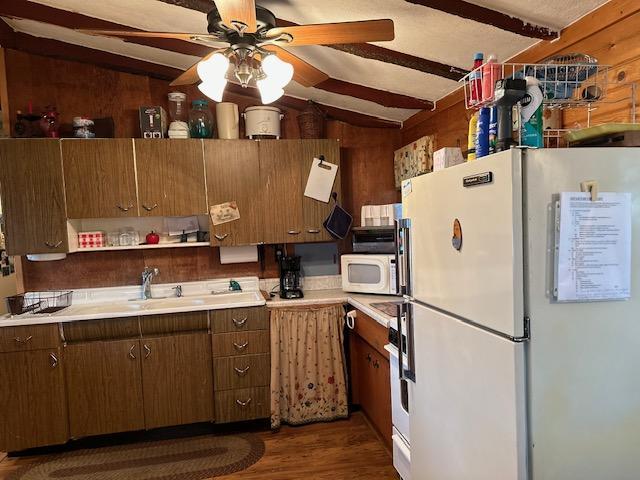 kitchen featuring white appliances, ceiling fan, vaulted ceiling with beams, dark hardwood / wood-style floors, and wood walls