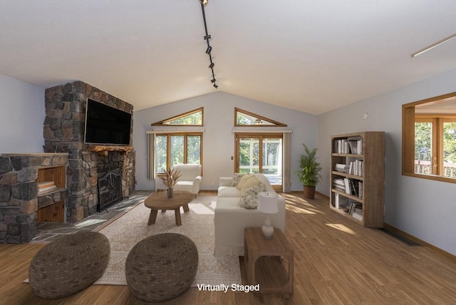 living room with wood-type flooring, a stone fireplace, vaulted ceiling, and rail lighting