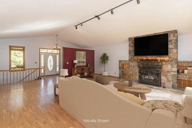 living room with lofted ceiling, a fireplace, track lighting, a chandelier, and light wood-type flooring