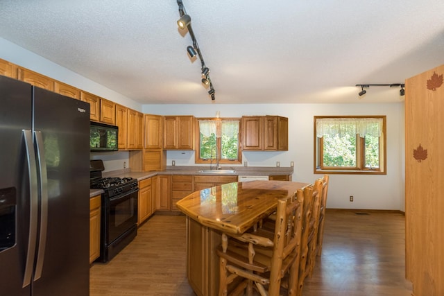 kitchen with sink, rail lighting, dark hardwood / wood-style floors, black appliances, and a textured ceiling