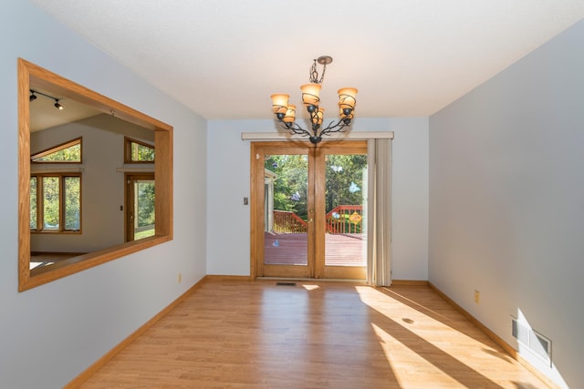 entryway with an inviting chandelier, light hardwood / wood-style floors, french doors, and a wealth of natural light