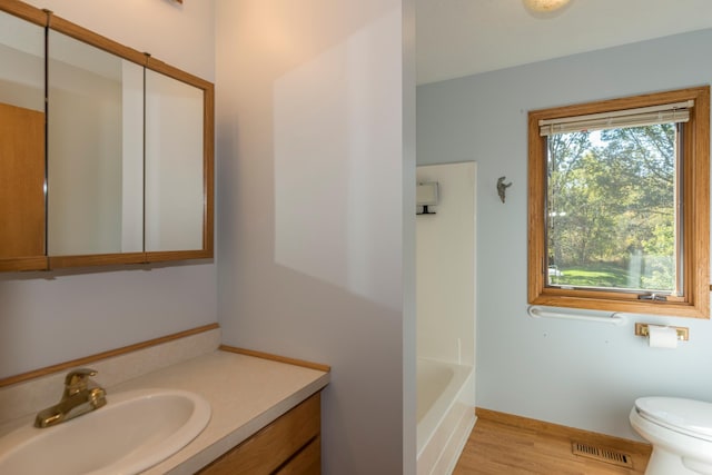 bathroom featuring toilet, vanity, a bath, and wood-type flooring