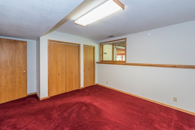 unfurnished bedroom featuring a textured ceiling, multiple closets, and carpet flooring