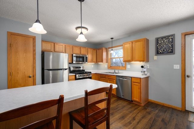 kitchen with dark wood finished floors, light countertops, hanging light fixtures, stainless steel appliances, and a sink