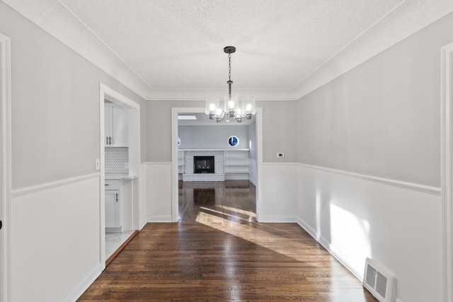 unfurnished dining area with dark wood-type flooring, a textured ceiling, a notable chandelier, and a fireplace