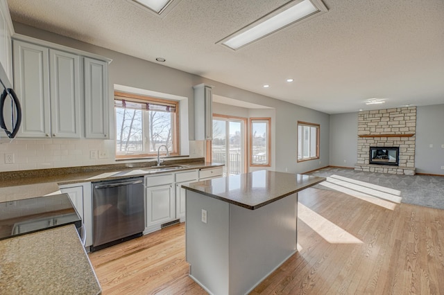 kitchen featuring a kitchen island, a stone fireplace, sink, stainless steel dishwasher, and light hardwood / wood-style flooring