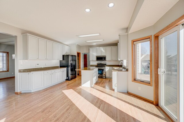 kitchen with sink, white cabinets, a center island, stainless steel appliances, and light wood-type flooring