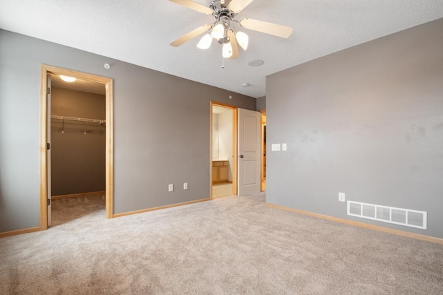 unfurnished bedroom featuring ceiling fan, a textured ceiling, light carpet, a walk in closet, and a closet