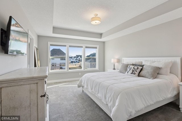 bedroom featuring carpet, baseboards, a textured ceiling, and a tray ceiling