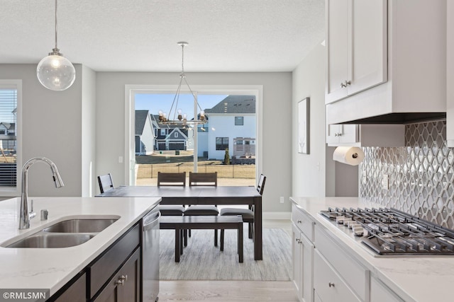 kitchen with sink, white cabinets, hanging light fixtures, light stone counters, and stainless steel appliances