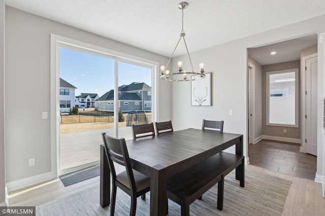 dining room with baseboards, a residential view, wood finished floors, an inviting chandelier, and a textured ceiling