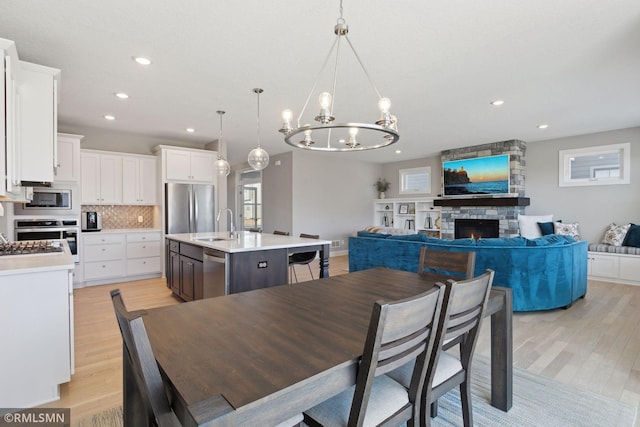 dining room with a stone fireplace, sink, and light wood-type flooring