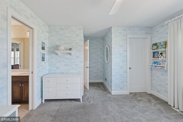 unfurnished bedroom with ceiling fan, light colored carpet, a textured ceiling, and ensuite bath