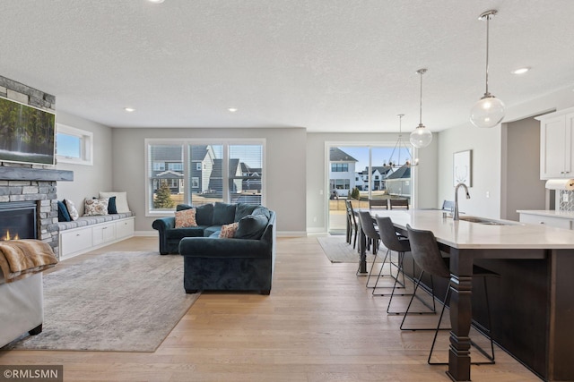 living room featuring light wood-style flooring, baseboards, a textured ceiling, and a stone fireplace