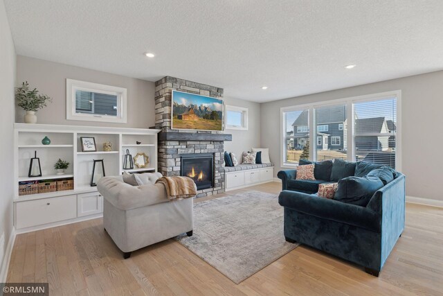 living area featuring recessed lighting, a stone fireplace, a textured ceiling, light wood-type flooring, and baseboards