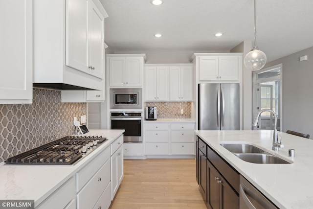 kitchen with white cabinets, light wood-style flooring, hanging light fixtures, stainless steel appliances, and a sink