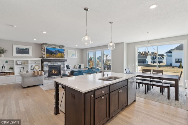 kitchen with a kitchen island with sink, open floor plan, light countertops, stainless steel dishwasher, and pendant lighting