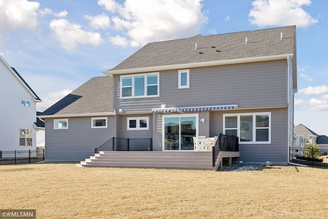 back of property featuring a shingled roof, a lawn, a deck, and fence