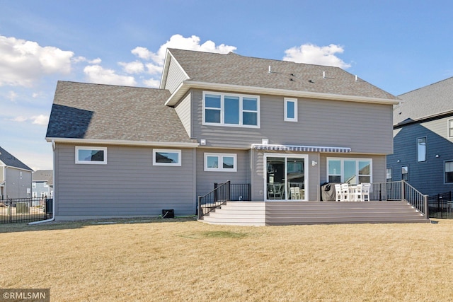 back of house featuring a deck, a shingled roof, and a lawn