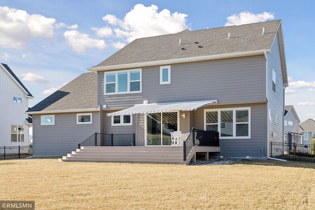 rear view of house with roof with shingles, a yard, and fence