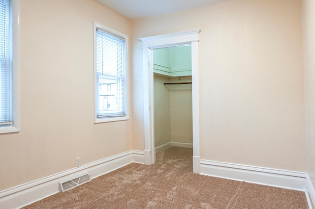 unfurnished bedroom featuring light carpet, a spacious closet, multiple windows, and a closet