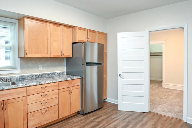 kitchen featuring wood-type flooring, stainless steel fridge, light brown cabinetry, and backsplash