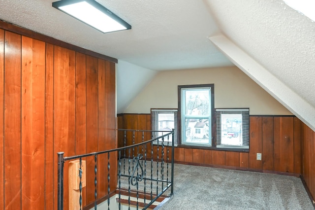 additional living space featuring lofted ceiling, wooden walls, a textured ceiling, and carpet flooring