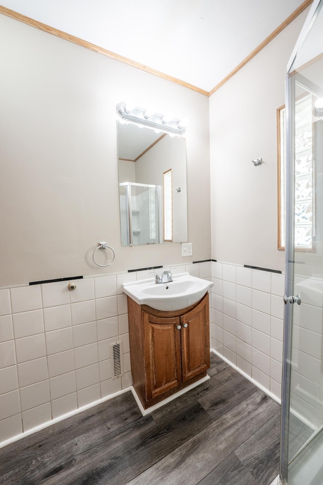 bathroom featuring wood-type flooring, tile walls, vanity, a shower with door, and crown molding