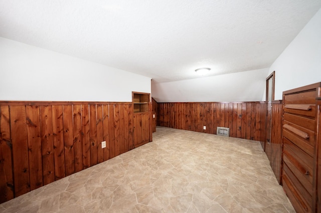 additional living space with vaulted ceiling, a textured ceiling, and wood walls