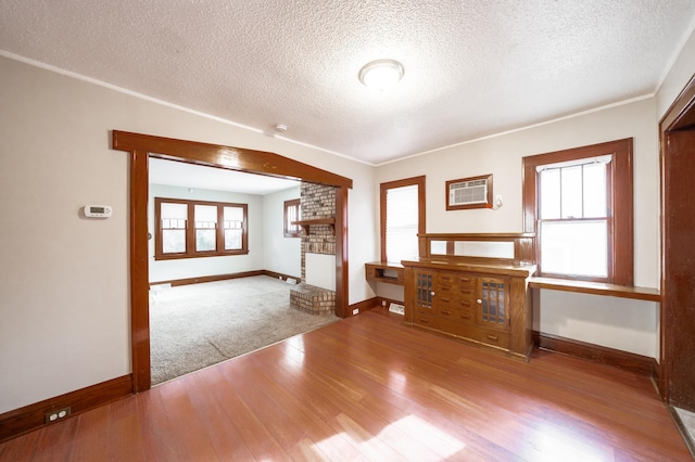 unfurnished living room featuring a wall mounted air conditioner, a fireplace, light hardwood / wood-style floors, and a textured ceiling