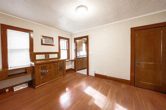 empty room featuring hardwood / wood-style flooring, a wall unit AC, crown molding, and a textured ceiling