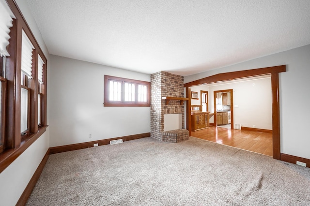 unfurnished living room featuring a brick fireplace, light colored carpet, and a textured ceiling