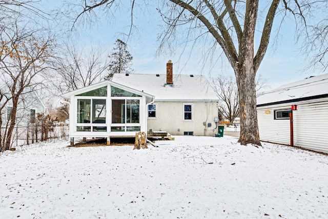 snow covered rear of property with a sunroom