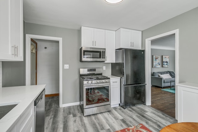 kitchen with stainless steel appliances, white cabinetry, light stone counters, and light hardwood / wood-style floors