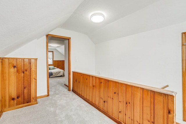 additional living space featuring lofted ceiling, wooden walls, and light colored carpet