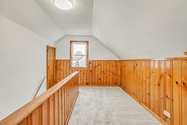 additional living space featuring lofted ceiling, light colored carpet, a textured ceiling, and wood walls