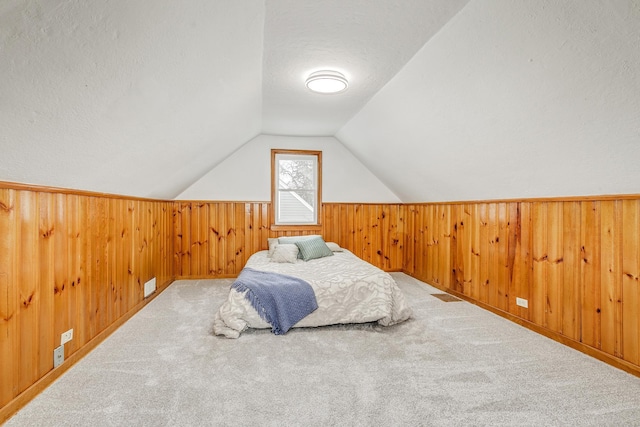 bedroom with lofted ceiling, wood walls, a textured ceiling, and carpet flooring